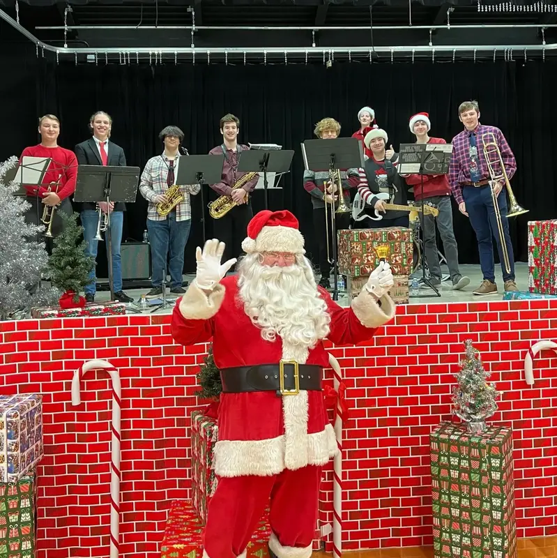 The Scholars on stage at a holiday event with Santa waving in front of the band