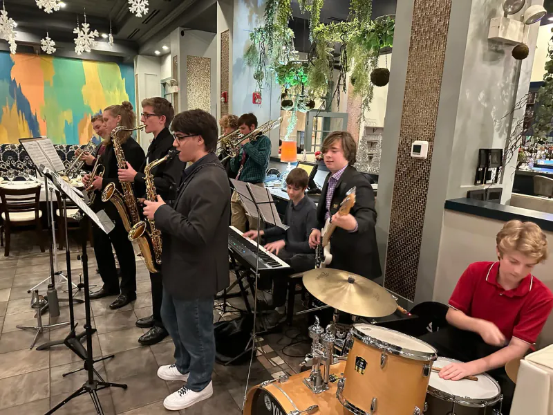 The Scholars playing inside a restaurant hung with paper snowflakes: saxophones, trumpets, and trombones, with keyboard, bass, and drums