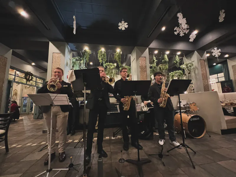 Trumpets and saxophones of The Scholars performing in a restaurant, with keyboard, bass, and drums behind them